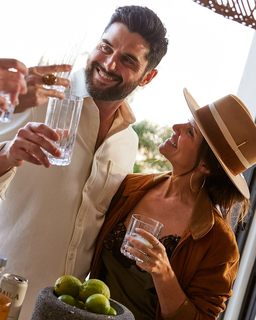 Three people enjoying drinks together outdoors, with bottles and limes on a table.